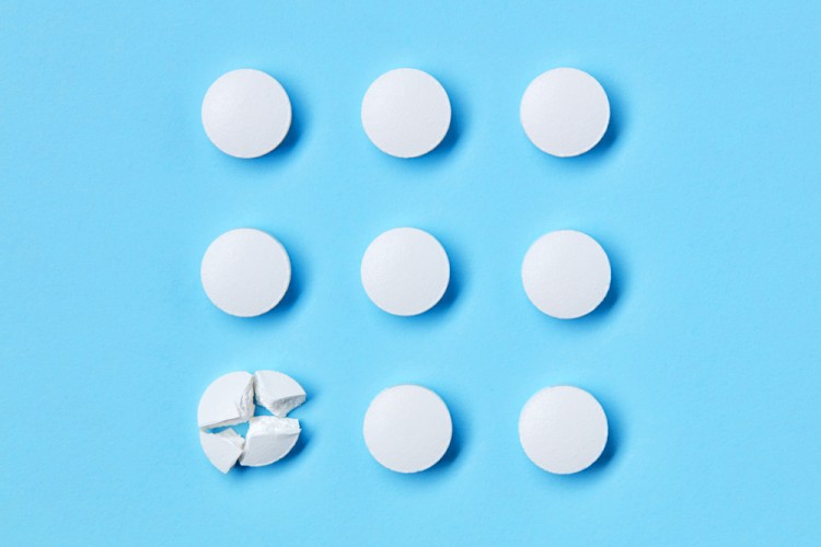 Round white medical pills arranged in square order and one of them is crushed into four parts. Pill splitting